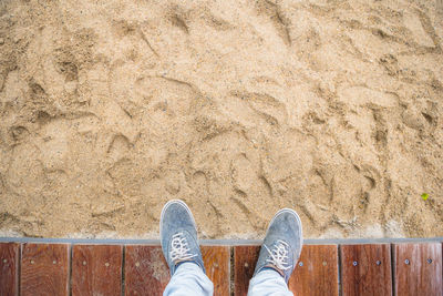 Low section of man standing on boardwalk by sandy beach