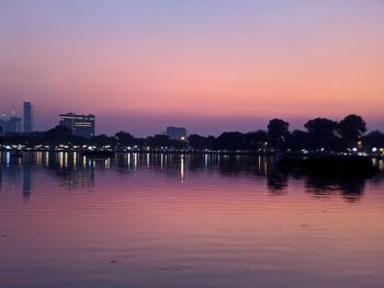 Scenic view of lake by illuminated buildings against sky during sunset