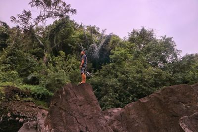 Side view of mid adult man standing on rock against trees