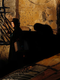 Side view of young man sitting against wall