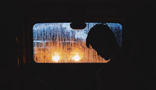 Rear view of silhouette man against window in dark room