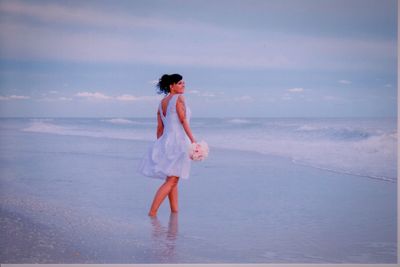 Woman holding bouquet while walking on shore at beach