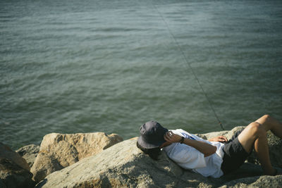 High angle view of man relaxing with hat on rocks by sea