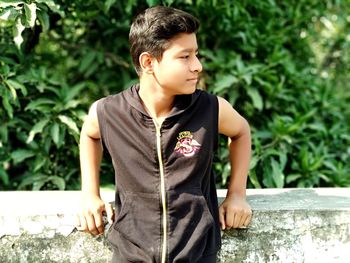 Boy looking away while standing against plants