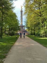 Male friends cycling on walkway in park against berlin victory column