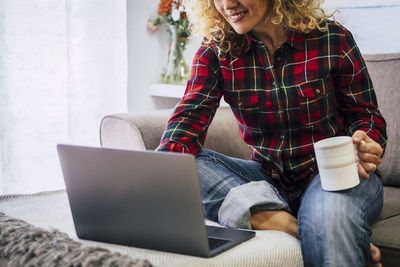 Midsection of woman using laptop while holding coffee cup