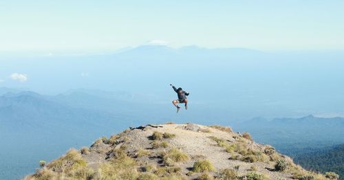 Happy mature man jumping on mountain against sky