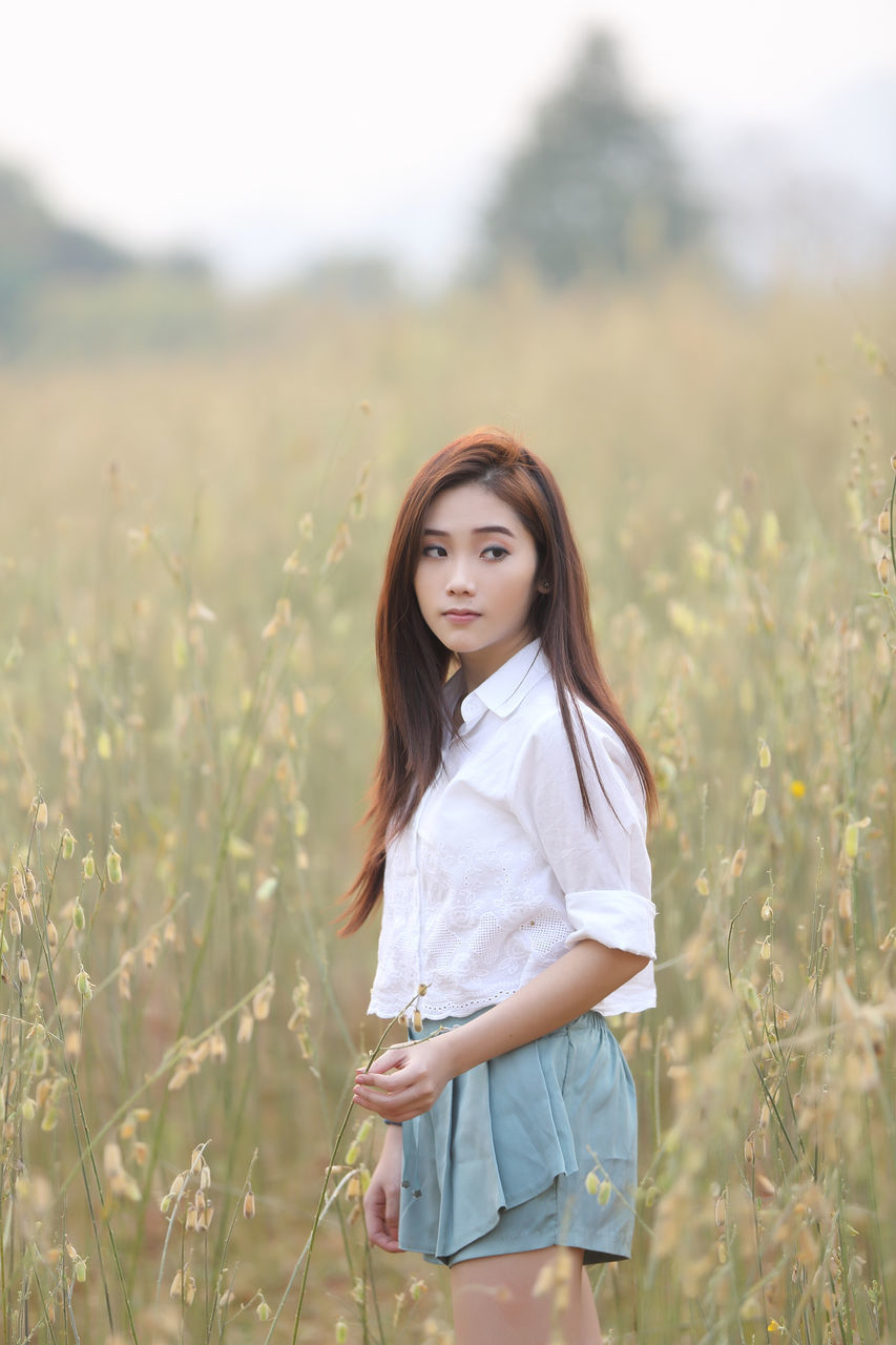 PORTRAIT OF WOMAN STANDING ON FIELD