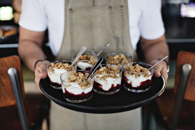 Midsection of owner holding dessert in tray while standing at counter in restaurant