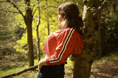 Side view of woman standing by trees in forest