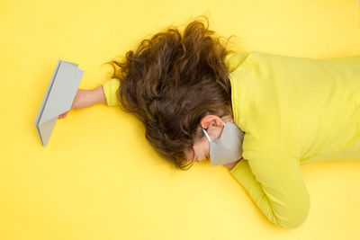 High angle view of girl lying down on yellow background