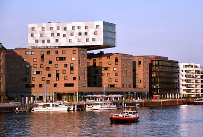 Boats in river by buildings in city against clear sky