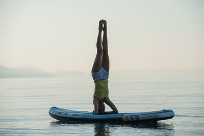 Full length of woman performing hand stand on paddleboard against sky
