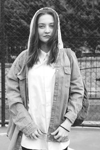 Portrait of young woman wearing hooded shirt while standing against gate