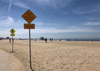 Road sign on beach against sky