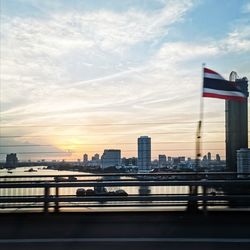 Bridge over city buildings against sky during sunset