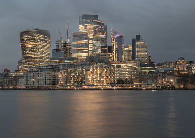 Illuminated buildings by river against sky at night