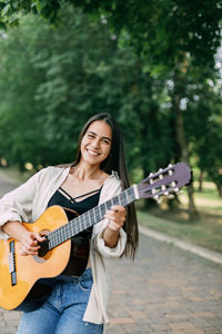 A beautiful girl plays the guitar, walks along the alley in the park. music, musician, guitar