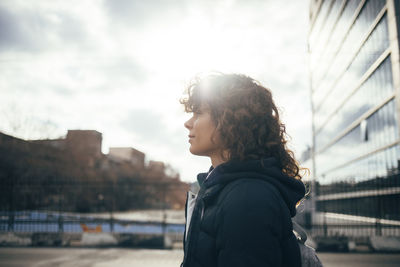 Mid adult woman looking away while standing by road at city