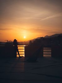 Silhouette man standing by railing against sky during sunset