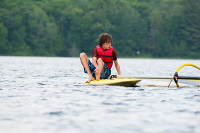 Teenage boy sitting on paddleboard in river