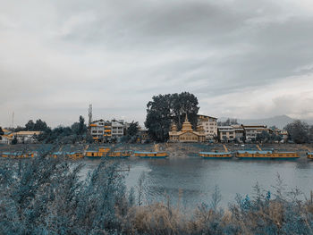 Buildings at waterfront against cloudy sky