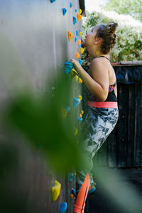 Side view of child in sportswear climbing wall with artificial rocks while training in gym and enjoying weekend