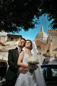 Wedding couple smiling while standing against buildings