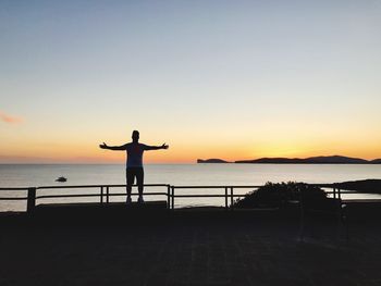 Silhouette man standing by sea against sky during sunset