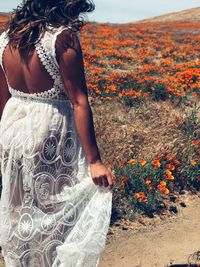 Rear view of woman in white dress standing by flowering field