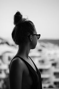 Side view of young woman wearing sunglasses standing against clear sky