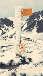 Road sign on snow covered mountain against sky