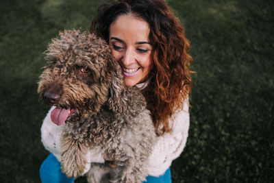 High angle view of smiling woman holding dog on grassy land