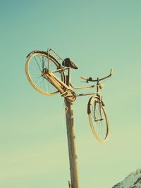 Low angle view of bicycle hanging on wooden post against clear sky