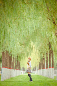 Side view of young woman standing on grass against trees