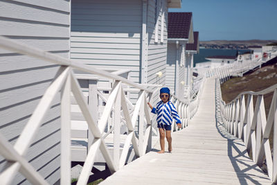 Boy child in a striped blue sailor jacket walks on the street among white wooden houses by the sea