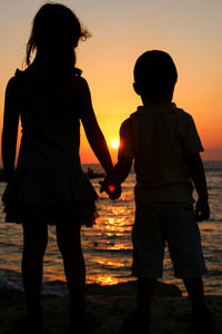 Silhouette friends standing at beach during sunset