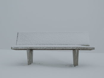 Empty bench on snow covered table against wall