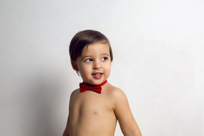 Child without a t-shirt sitting on a white background with a red bow tie