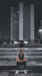 Full length portrait of young man sitting against building in city