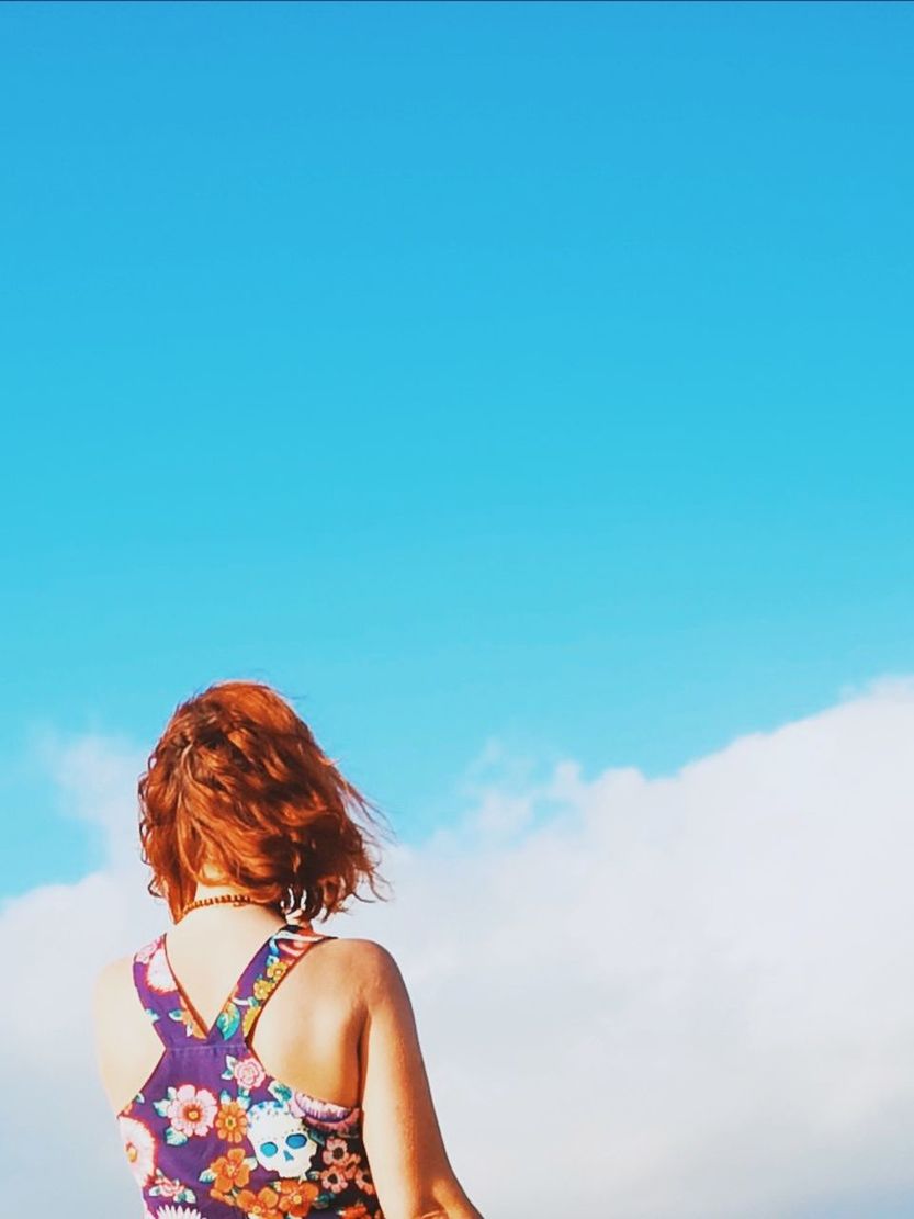 sky, one person, rear view, hairstyle, cloud - sky, leisure activity, women, day, nature, real people, lifestyles, hair, copy space, redhead, blue, standing, sunlight, adult, long hair, outdoors, contemplation, floral pattern