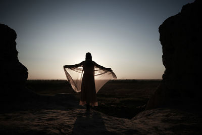 Rear view of silhouette man standing on rock against sky