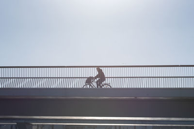 Low angle vie of man riding bicycle on bridge against clear sky during sunny day