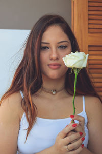 Portrait of smiling woman holding rose at home