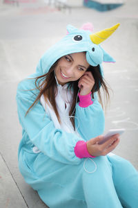 Smiling young woman in costume using phone while sitting outdoors