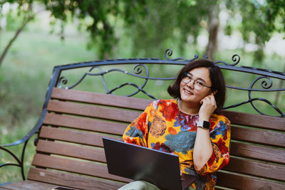 Young woman using laptop while sitting on bench