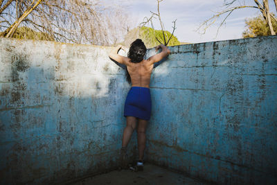 Rear view of shirtless woman standing against wall