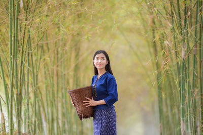 Young woman wearing traditional clothing while holding basket in bamboo grove