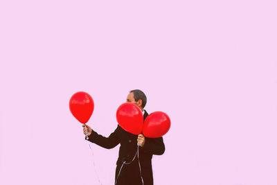 Rear view of woman with umbrella standing against pink background