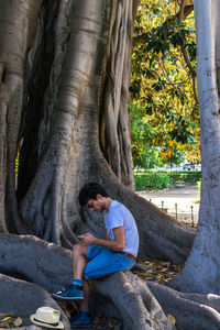 Side view of man sitting on tree root